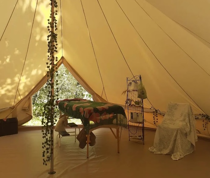 Open-air massage tent with wellness plants and treatment table, Détente et Clapotis campsite